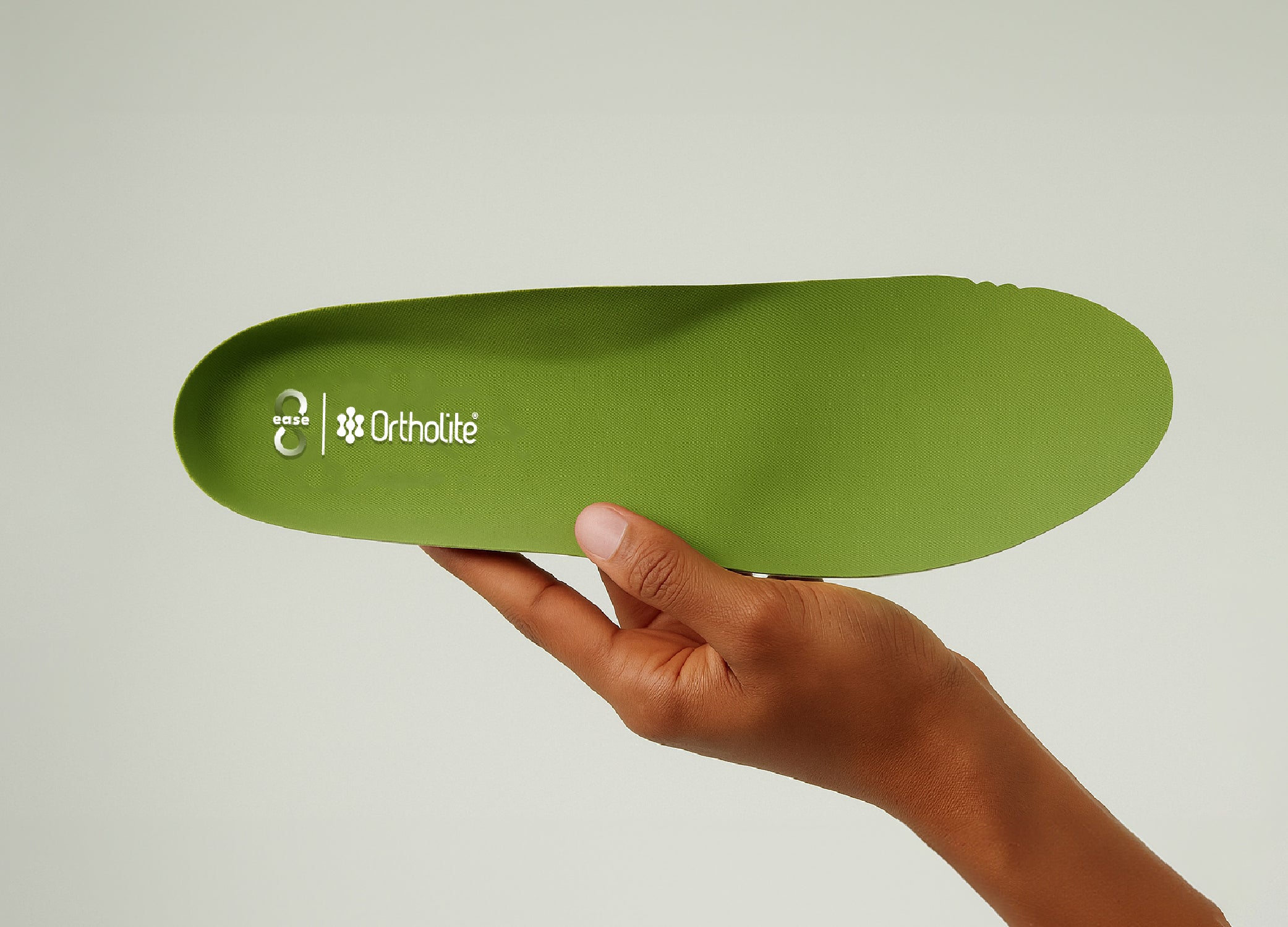 Hand holding a green Ortholite insole with 8ease branding, shown against a plain light background